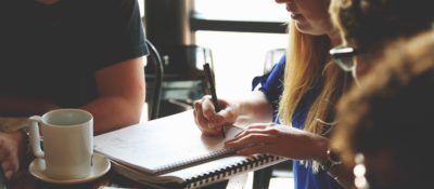 People around a table at a coffee shop. Discussing work, pen and paper, coffee mugs.