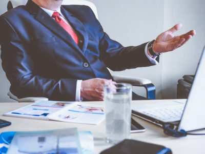 Image of man sitting at office desk with hand extended forward as if he's gesturing to a person he is speaking to