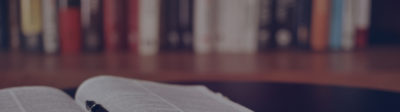 An open book on a desk with a pen resting in the middle of the pages