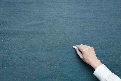 A hand holding a piece of chalk against a chalkboard