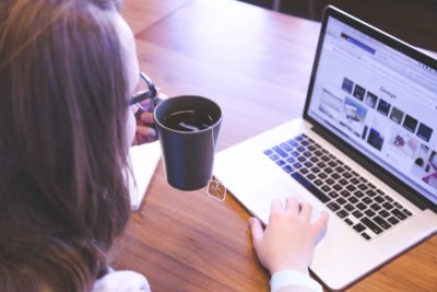 A person browsing on a laptop, holding a cup of tea