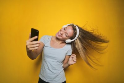 A woman dancing while looking at her cellphone and wearing headphones