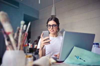 A woman sitting at her laptop, looking at her cellphone