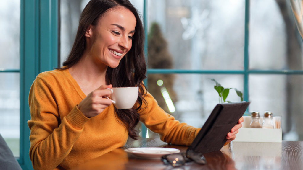 A woman looking at her tablet, smiling, holding a cup of coffee