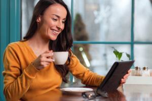 A woman looking at her tablet, smiling, holding a cup of coffee