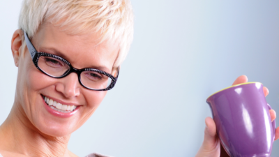 woman smiling with a cup of tea looking at resources on her computer