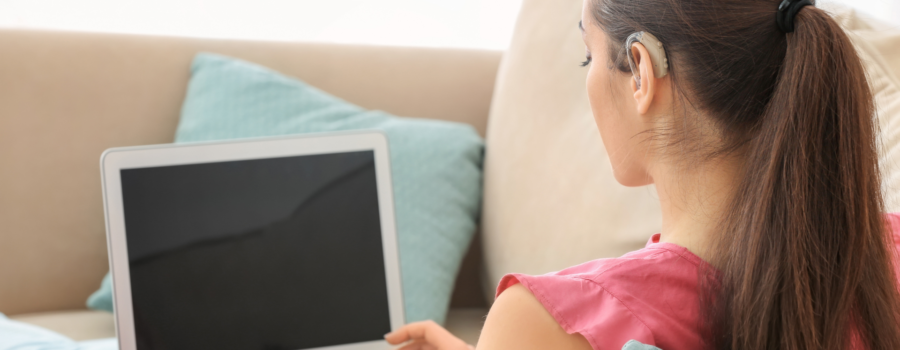 girl with hair pulled back showing hearing aid with laptop on her lap