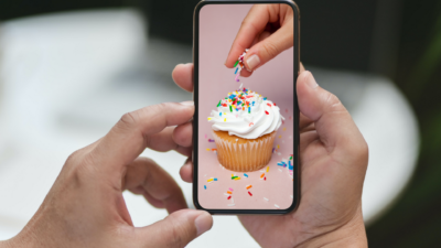 person sprinkling a cupcake, person watching it on their phone. 