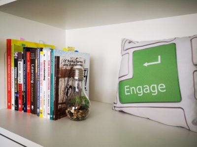 book shelf with several books and a pillow that says engage