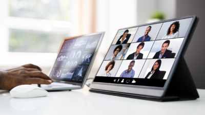 image of 2 computers with hand on one and mouse beside showing several people on the screens