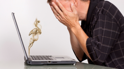 computer crashed man upset, holding hands over face, and smoke coming out of computer