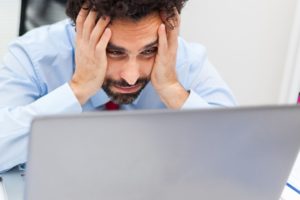 Computer crashed, man holding hands on face looking at computer