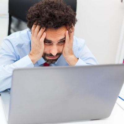 Computer crashed, man holding hands on face looking at computer