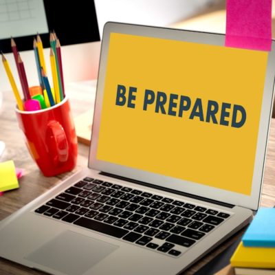 image of laptop on desk that says be prepared on the screen beside a mug of pencils 