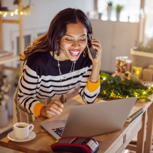 image of woman in front of laptop with a coffee in a decorated room having fun at a hybrid holiday party