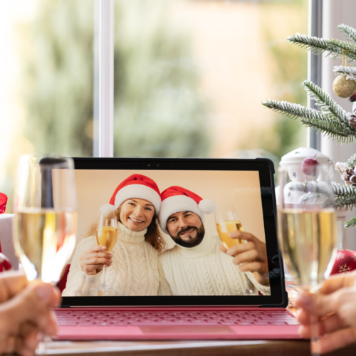 image of a couple in santa hats on a laptop screen with champagne toasting people in front of the laptop for a hybrid holiday party