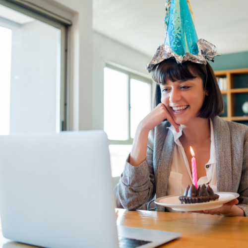 hybrid celebration online birthday cake and festive hat woman looking at computer