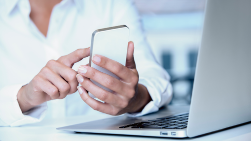 person holding phone and completing an evaluation, laptop on desk