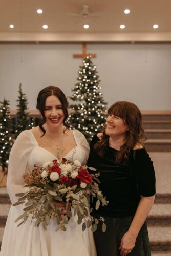 my daugher and I, she is wearing a wedding gown and holding flowers, I am looking at her smiling, there are holiday lit trees behind us