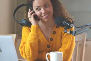 woman in yellow sweater listening to a recording in a headset, mic and laptop with a mug on table