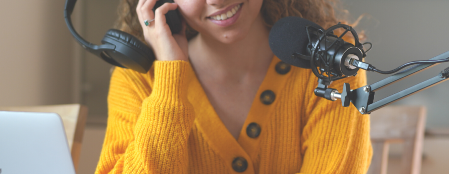 woman in yellow sweater listening to a recording in a headset, mic and laptop with a mug on table