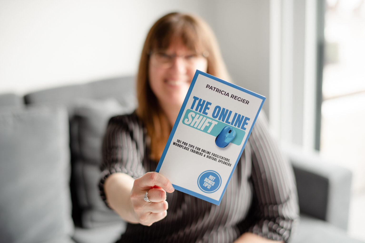 Patricia in background with a black and white stripped shirt, holding her book The Online Shift in the foreground.