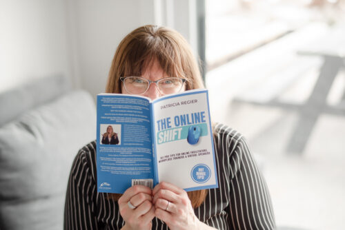 Patricia in background with a black and white stripped shirt, peeking behind her book The Online Shift in the foreground.
