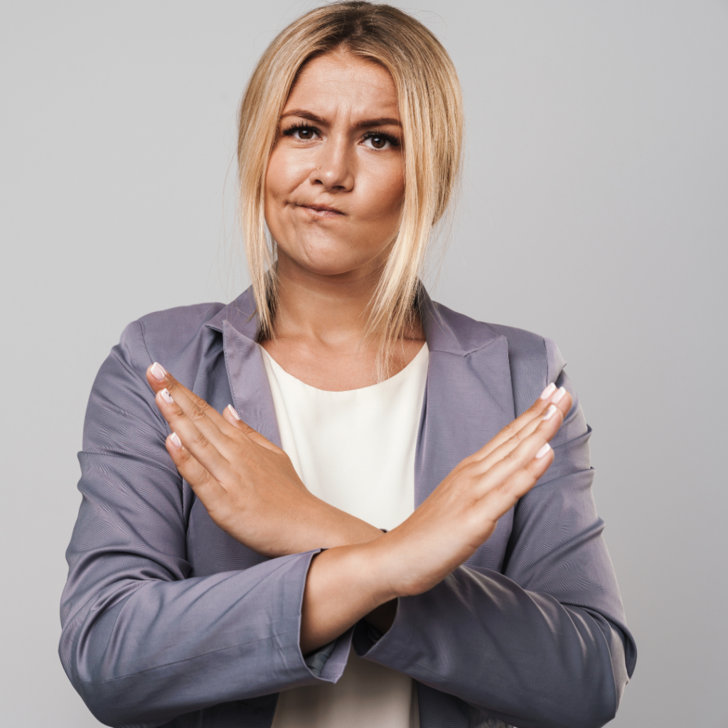 White woman with blond hair, face expression mouth to the side, and arms in an X formation with hands to demonstrate No. Person wearing grey suite jacket and white top. No to WebEx Expression.
