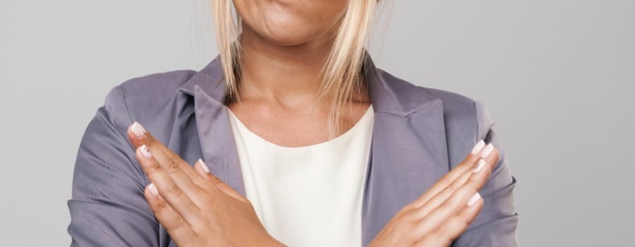 White woman with blond hair, face expression mouth to the side, and arms in an X formation with hands to demonstrate No. Person wearing grey suite jacket and white top. No to WebEx Expression.