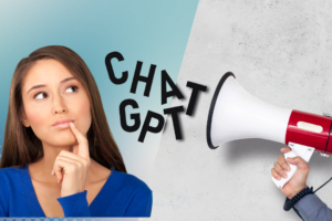 Woman with brown hair and a blue top, finger by mouth thinking and looking at the words CHAT GPT coming out of a megaphone