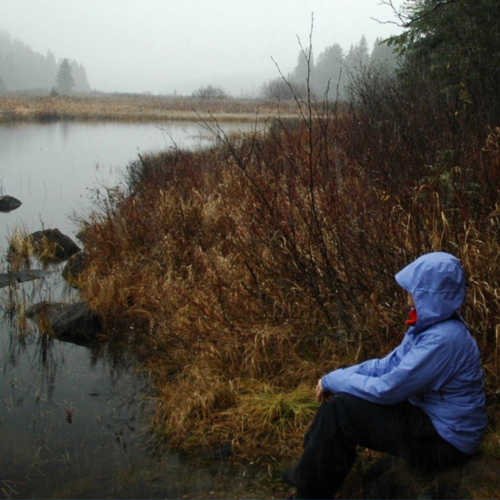 Personal Photo: Patricia in a blue rain jacket sitting hear a foggy lake. Self Care