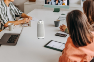 People in a meeting onsite and hybrid blended audience online. The Meeting Owl is on the table.