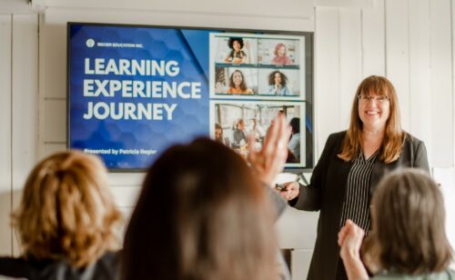 Patricia speaking to a workshop, heads of people in the foreground, TV with slide and words Learning Experience Journey in the background.