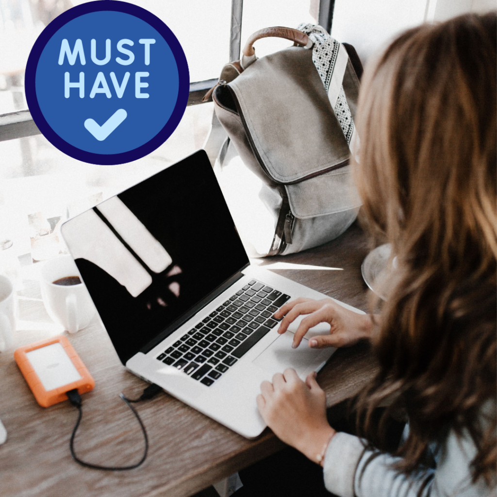 Person typing on a laptop while travelling, with backup drive.